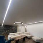 Interiér obytného domu s inštalovaným napínacím stropom v bielom, matnom prevedení, v kombinácii s lineárnym osvetlením a dominantným kruhovým LED svietidlom