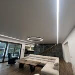 Detail lineárneho osvetlenia aplikovaného v strope s matnou bielou fóliou, v strede s dominantným kruhovým svietidlom