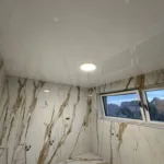 Biely lesklý napínaný strop v kúpeľni rodinného domu s mramorovým dizajnom obkladu