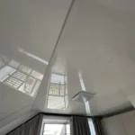 Detailný záber napínaného stropu v podkrovnej izbe s bielou lesklou fóliou a jedným stropným svietidlom