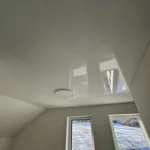 Lesklý napínaný strop s jedným stropným LED svietidlom nainštalovaný v podkroví rodinného domu