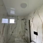 Moderná kúpeľňa v rodinnom dome s mramorovým obkladom s dizajnovými čiernymi doplnkami a inštalovaným napínacím stropom