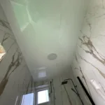 Biely napínací strop v modernej kúpeľni obloženej mramorovým obkladom